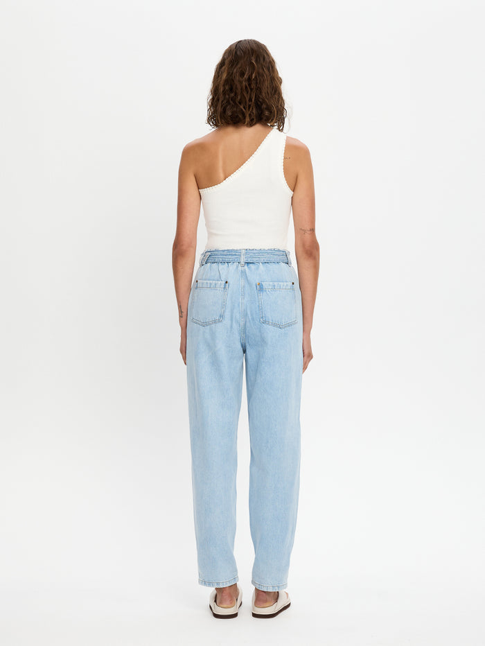 Woman wearing light blue jeans and a white one-shoulder top on a white background