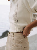 Close-up of a person wearing a white knit sweater and beige pants with a blurred background