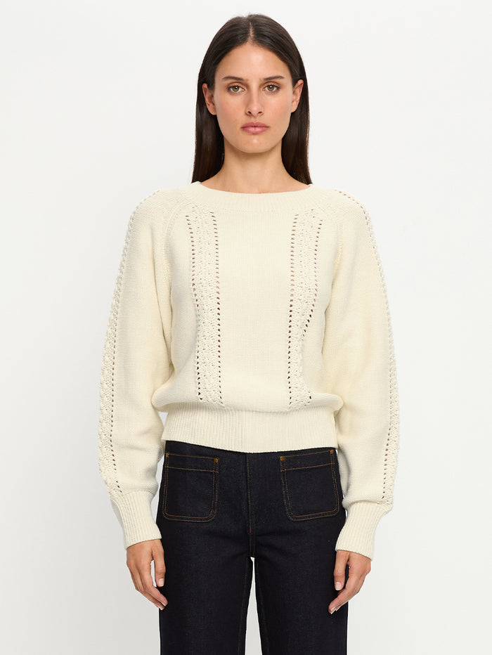 Woman wearing a cream sweater and dark jeans against a white background