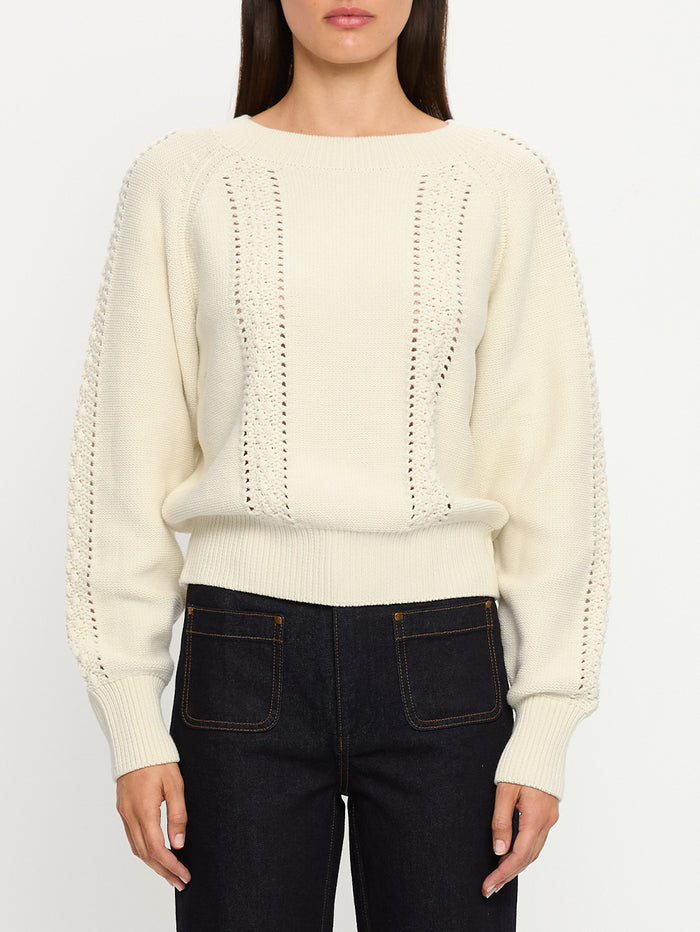 Person wearing a cream sweater with a textured pattern and dark jeans on a white background