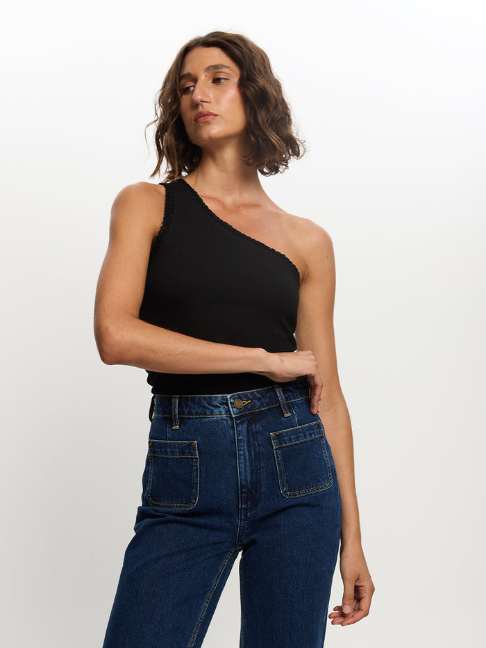 A woman wearing a black one shoulder tank top and blue jeans.