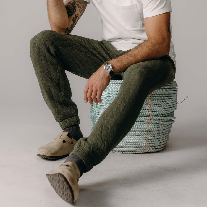 fit model sitting on a rope wearing The Quilted Apres Pant in Heather Fatigue Olive Jersey