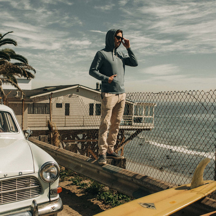 fit model balancing on a roadside railing in The Apres Pant in Khaki Double Cloth while lookng out at the ocean
