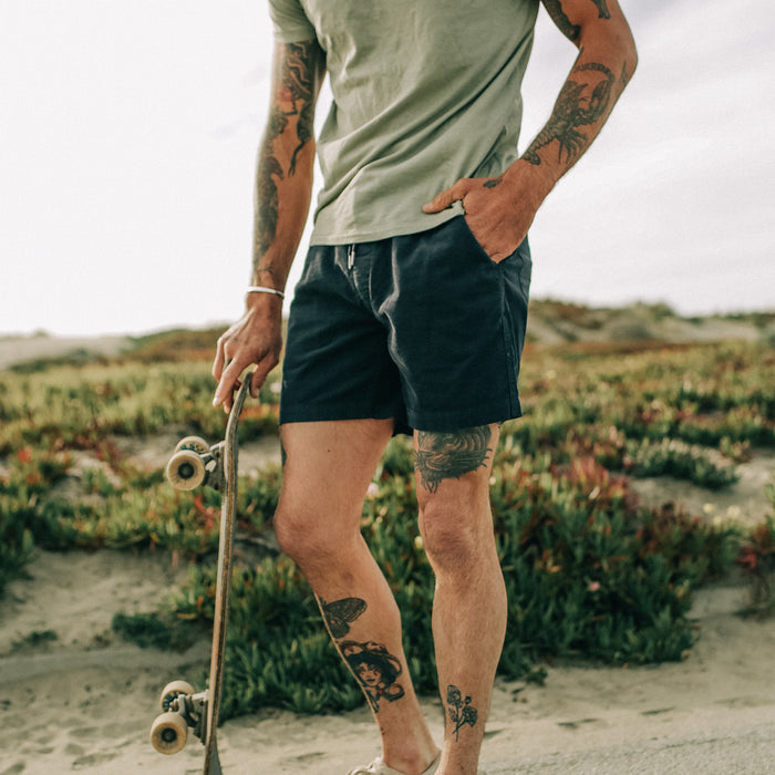 fit model posing in The Après Short in Dark Navy Pinwale while holding a skateboard