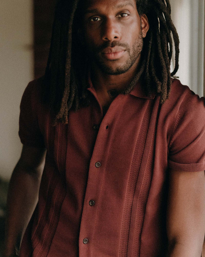 fit model leaning against the wall wearing The Button Down Polo in Dried Cherry Stripe