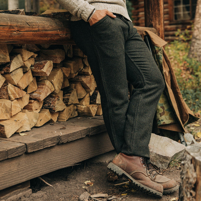 fit model wearing The Camp Pant in Dark Moss Wool, sitting against some logs
