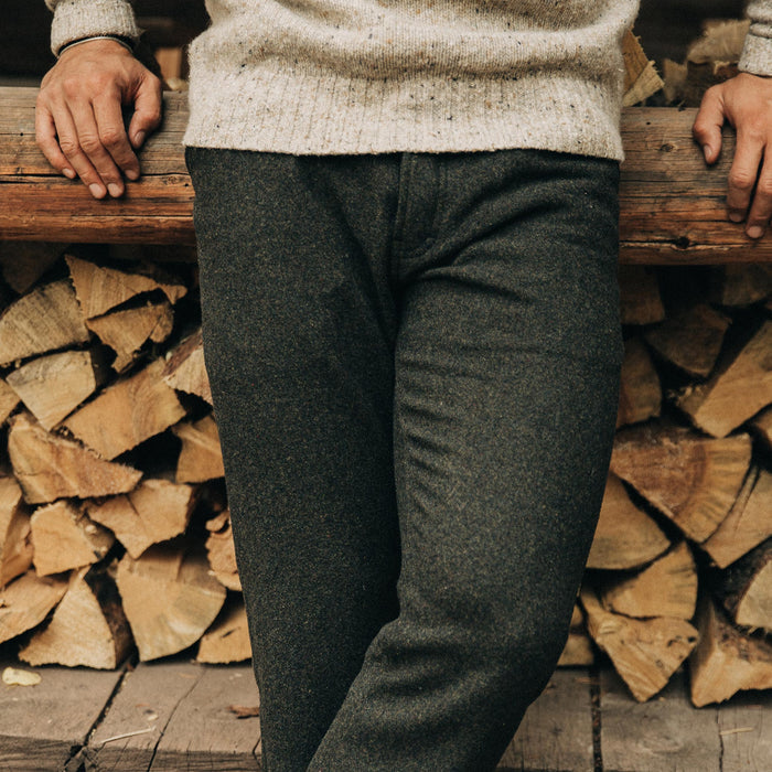 fit model wearing The Camp Pant in Dark Moss Wool, sitting against wood