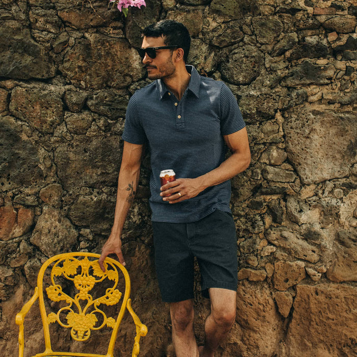 fit model wearing The Camp Short in Navy Herringbone, holding beer, next to yellow chair