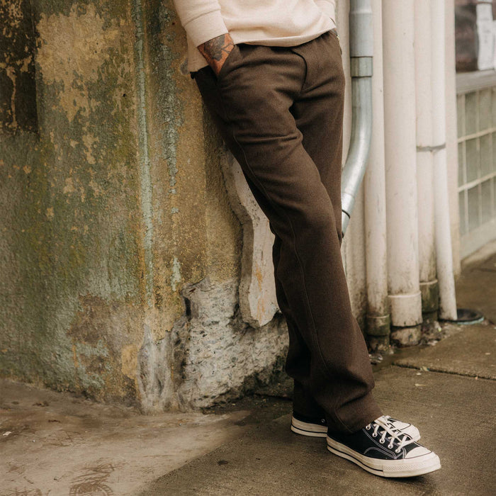fit model leaning against the wall wearing The Carnegie Pant in Army Herringbone Wool