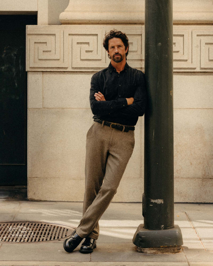 fit model leaning against a pole wearing The Carnegie Pant in Gravel Herringbone Wool