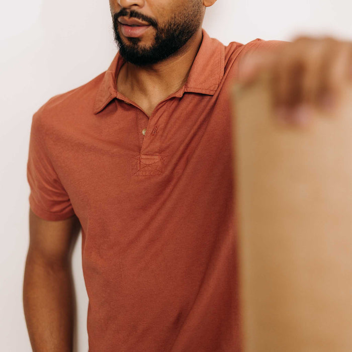 fit model holding a wall wearing The Cotton Hemp Polo in Fired Clay
