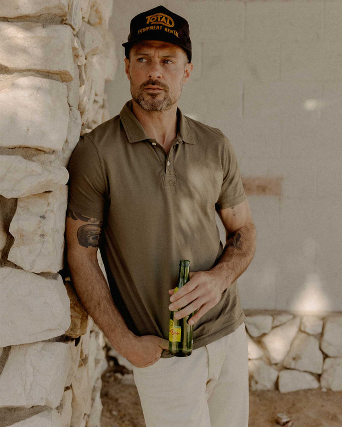 fit model leaning against the wall wearing The Cotton Hemp Polo in Olive