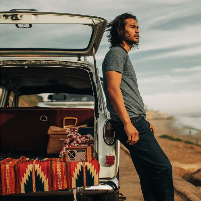 fit model leaning against a car wearing The Cotton Hemp Tee in Slate and Navy Stripe