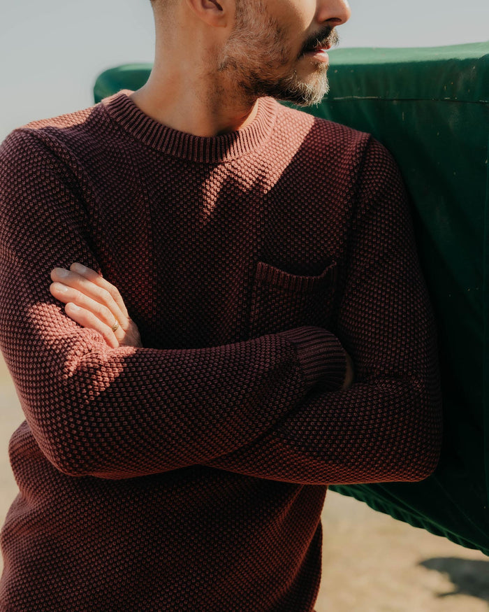 fit model leaning against the wall wearing The Crawford Crew Sweater in Dried Cherry