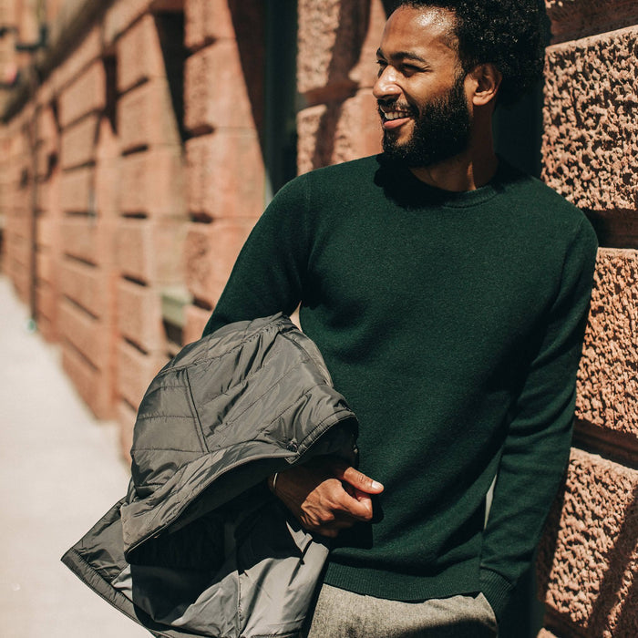 fit model wearing The Double Knit Sweater in Forest, holding jacket, looking left
