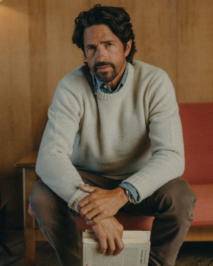 fit model sitting wearing The Eastmoor Sweater in Heather Ivory Wool