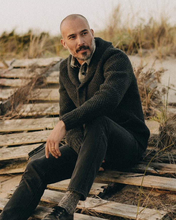 fit model sitting wearing The Fisherman Shawl Cardigan in Heather Coal Merino