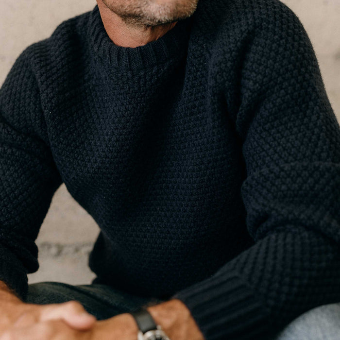 fit model sitting wearing The Fisherman Sweater in Dark Navy Merino