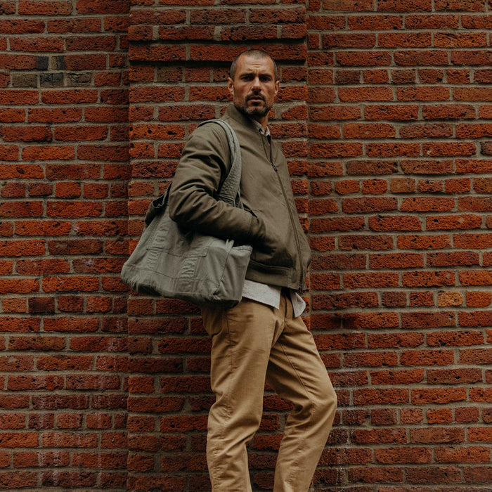 fit model leaning against the wall wearing The Foundation Tote in Organic Smoked Olive