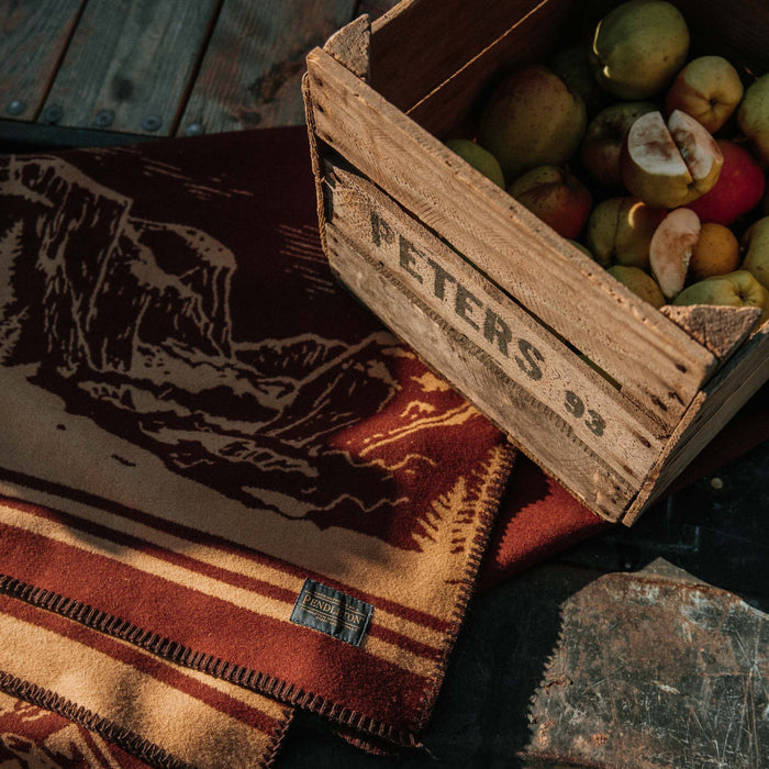The Golden State Blanket in Rust laying on the ground next to apple box | fit model