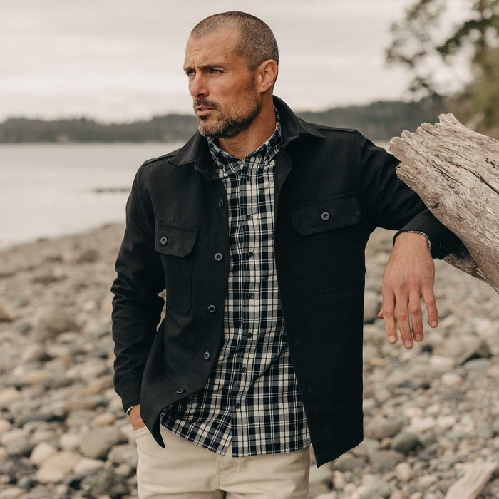 fit model leaning against a log wearing The Good Acre Forge Overshirt in Black Canvas