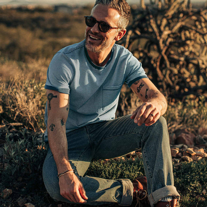 our fit model sitting down and wearing The Heavy Bag Ringer in Royal Blue Stripe out in the desert at sunset