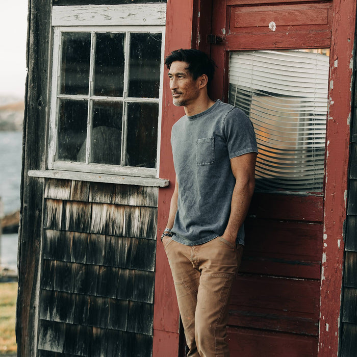 fit model wearing The Heavy Bag Tee in Charcoal, standing next to red door