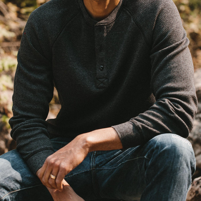 fit model sitting on a log stump in The Heavy Bag Waffle Henley in Coal