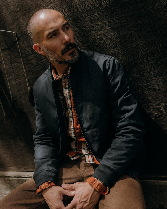 fit model sitting wearing The Insulated Bomber Jacket in Dark Navy Dry Wax