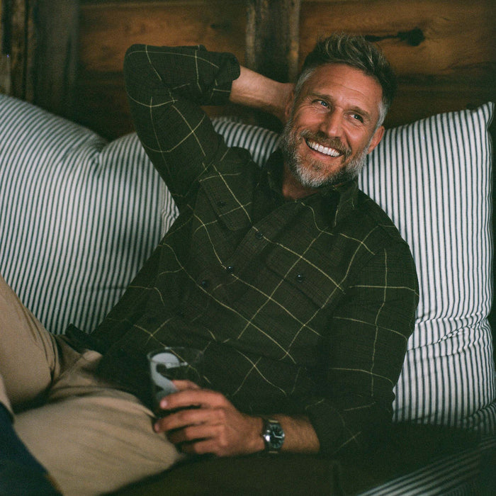 fit model sitting wearing The Ledge Shirt in Olive Plaid