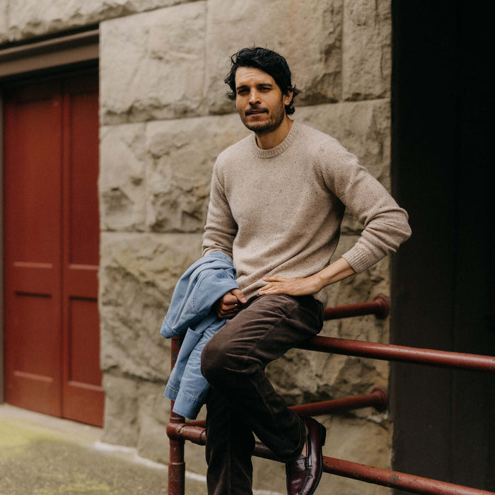 fit model leaning against a railing wearing The Lodge Sweater in Sand Donegal