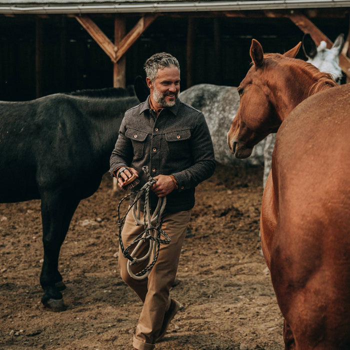 fit model wearing The Long Haul Jacket in Wool Beach Cloth—walking near horses