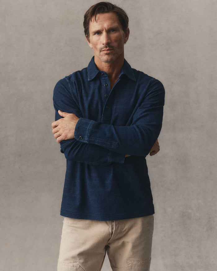fit model leaning against a table wearing The Long Sleeve Polo in Indigo Knit Stripe
