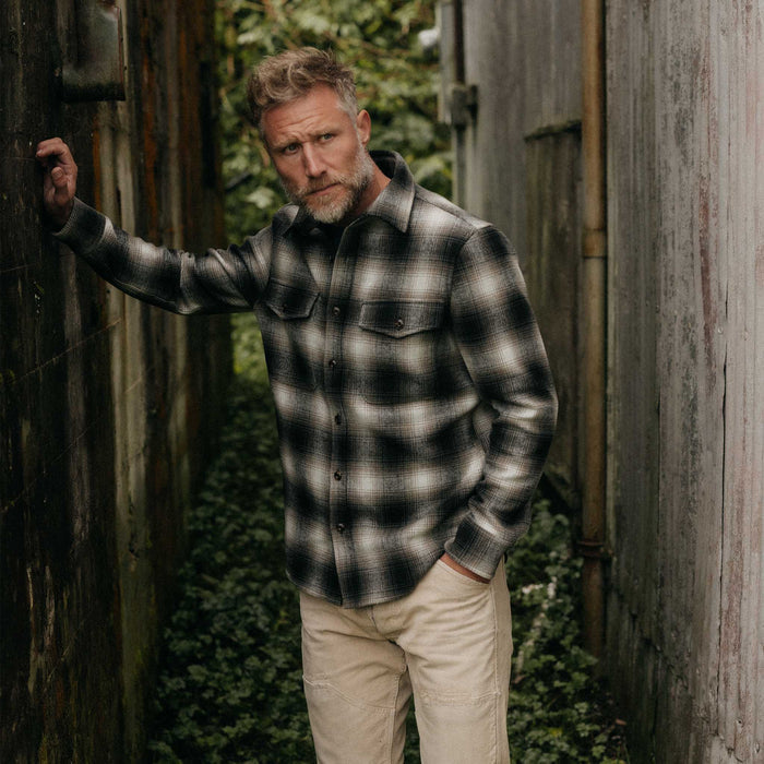 fit model leaning on the wall wearing The Maritime Shirt Jacket in Olive Plaid