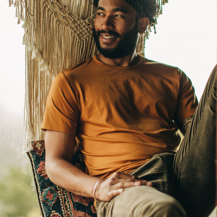 fit model wearing The Merino Tee in Heather Saffron, sitting, looking left