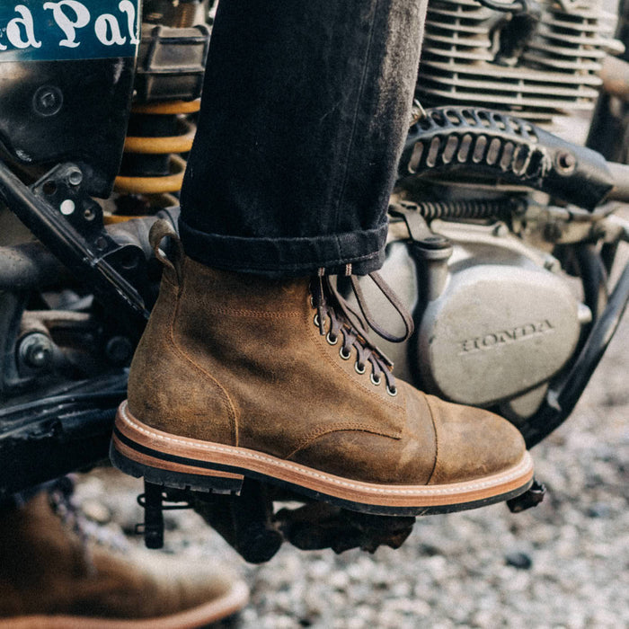 fit model wearing The Moto Boot in Golden Brown Waxed Suede while on a motorbike