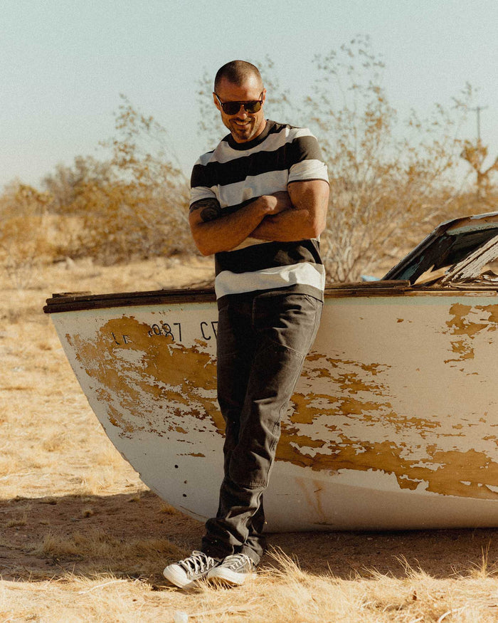 fit model leaning against a boat wearing The Organic Cotton Shop Tee in Faded Black Stripe