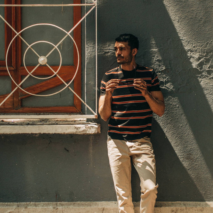 fit model wearing The Organic Cotton Tee in Coal and Rust Stripe, against wall