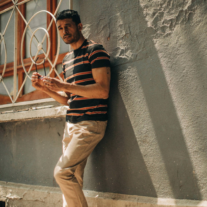 fit model wearing The Organic Cotton Tee in Coal and Rust Stripe, against wall