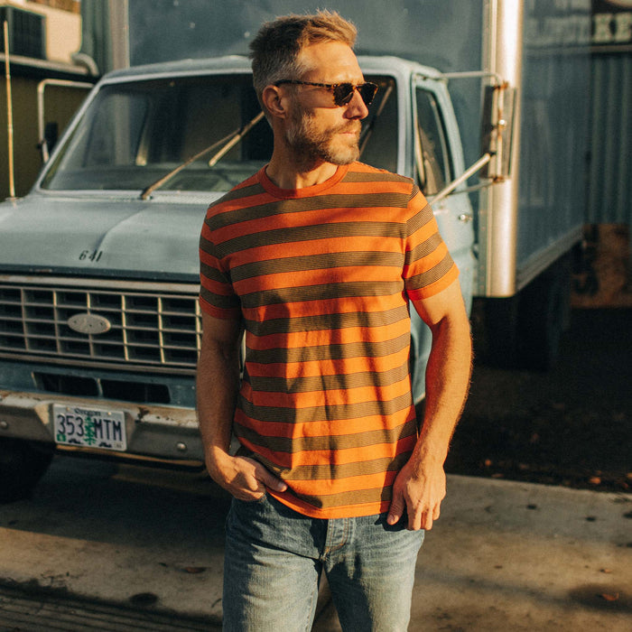 fit model wearing The Organic Cotton Tee in Rust Stripe in front of a blue truck