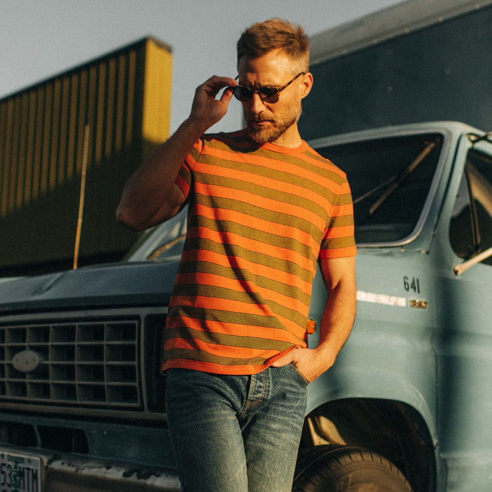 fit model posing by a blue pickup in The Organic Cotton Tee in Rust Stripe