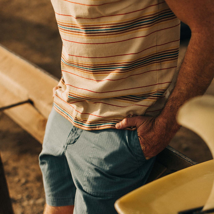 fit model leaning against a surfboard in The Organic Cotton Tee in Sand Stripe