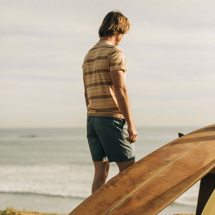 fit model standing by a surfboard in The Organic Cotton Tee in Sand Stripe