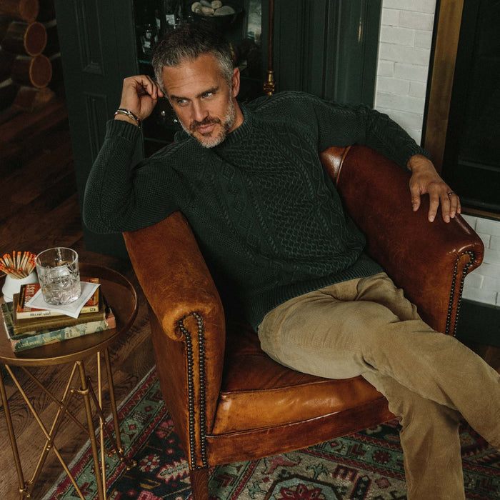 fit model wearing The Orr Sweater in Charcoal on an armchair