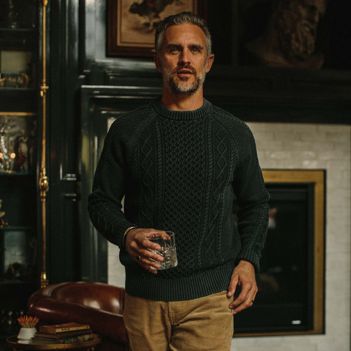 fit model wearing The Orr Sweater in Charcoal in front of a fireplace