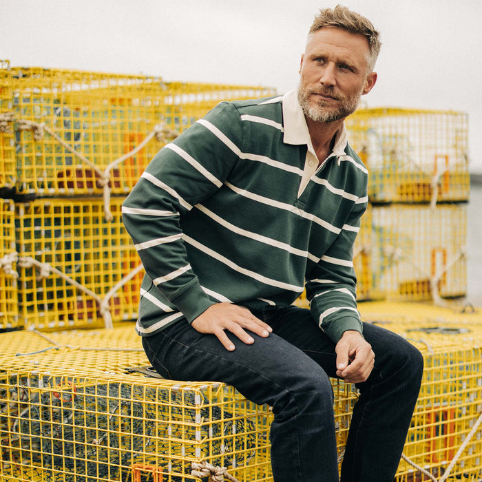 fit model sitting on fishing boxes wearing The Rugby in Dark Forest Stripe