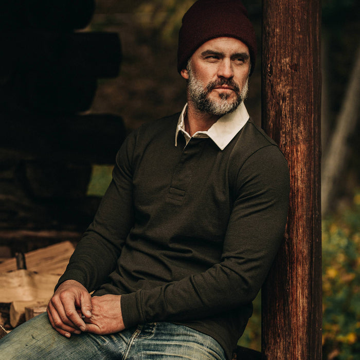 fit model wearing The Rugby Shirt in Cypress, resting against wood beam
