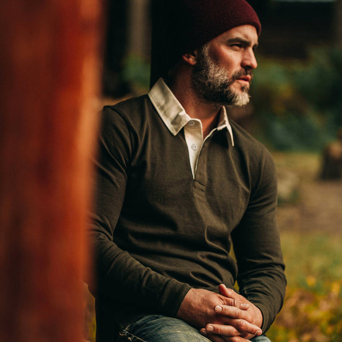 fit model wearing The Rugby Shirt in Cypress, resting against wood beam