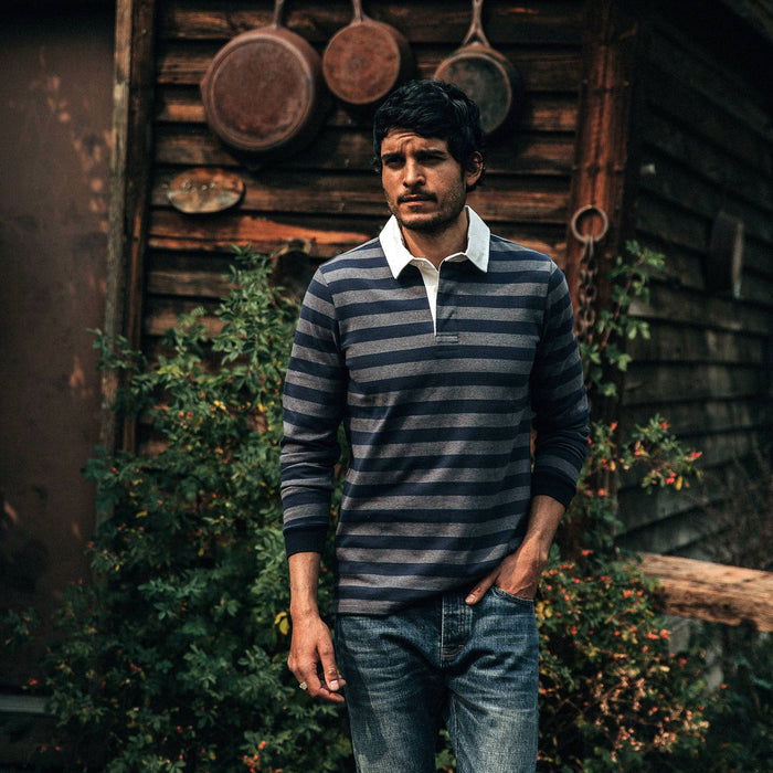 fit model wearing The Rugby Shirt in Navy Stripe, walking near cabin