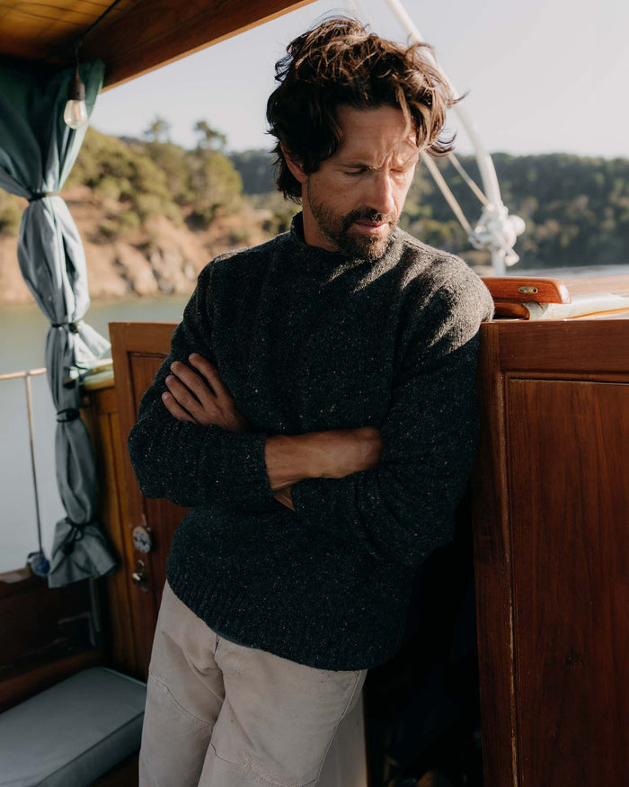 fit model leaning against the wall wearing The Seafarer Sweater in Charcoal Donegal